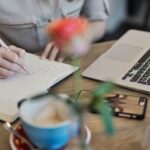 Content - Person Writing On A Notebook Beside Macbook