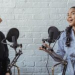 Host - Smiling African American female guest gesticulating while having interview with journalist sitting near mic