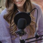 Hosting - Smiling woman recording podcast on microphone with laptop