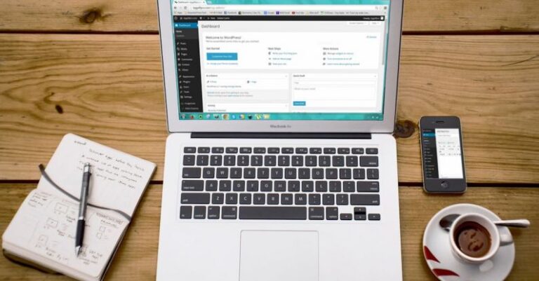 WordPress - Turned-on Macbook Air Beside Black Iphone 4, Cup of Tea, and Notebook on Brown Wooden Surface